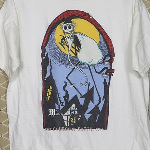 Puede incluir: Camiseta blanca con un estampado gr&aacute;fico de un personaje de dibujos animados disfrazado de fantasma. El personaje est&aacute; de pie en un edificio con una luna en el fondo. El texto "The Church of Satin.com" est&aacute; impreso en la parte inferior del gr&aacute;fico.