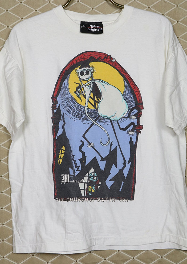 Puede incluir: Camiseta blanca con un estampado gr&aacute;fico de un personaje de dibujos animados disfrazado de fantasma. El personaje est&aacute; de pie en un edificio con una luna en el fondo. El texto "The Church of Satin.com" est&aacute; impreso en la parte inferior del gr&aacute;fico.