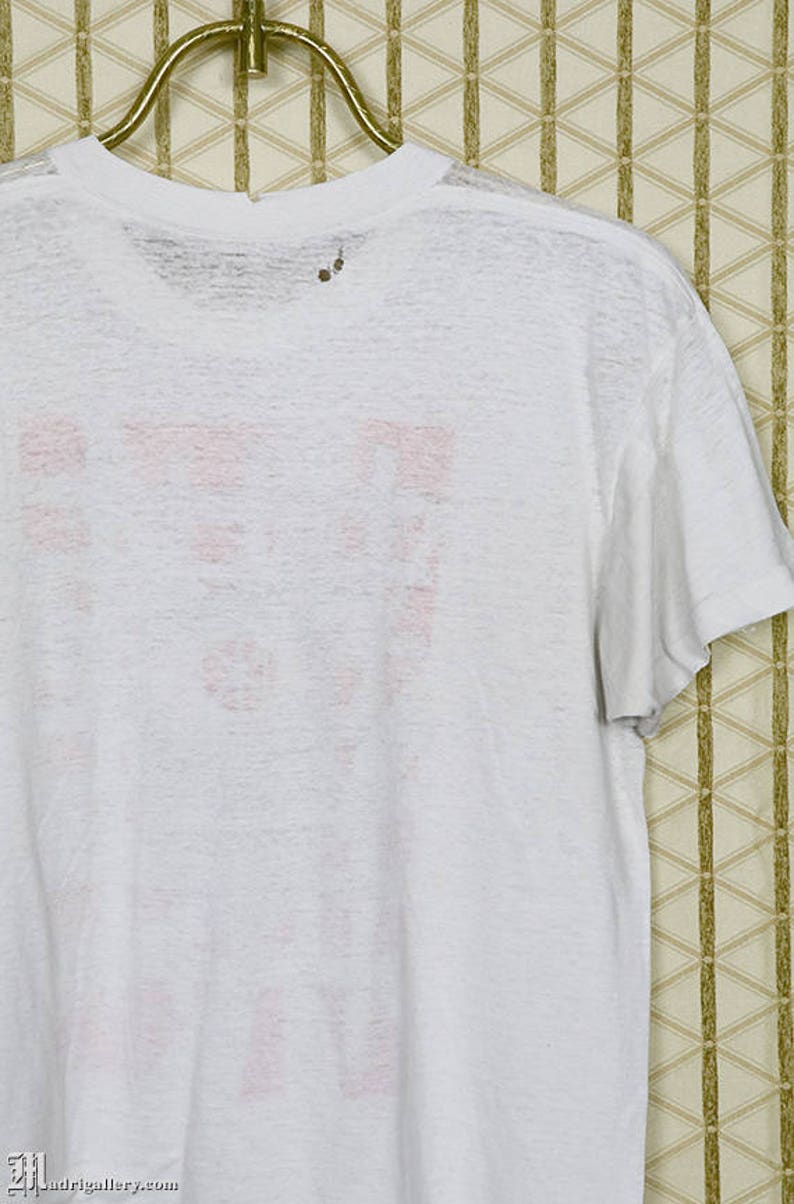 May include: White t-shirt with a faded pink graphic on the back. The graphic is a logo with the text "F.U.N."