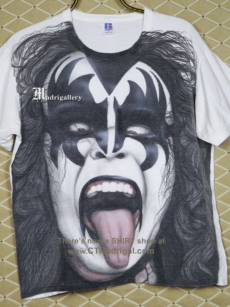 May include: White t-shirt featuring a black and white image of a person with long black hair and a face painted with black and white makeup. The person is wearing a black and white costume. The text "There's now a SHIRT shop at www.CTMadrigal.com" is printed on the bottom of the shirt.