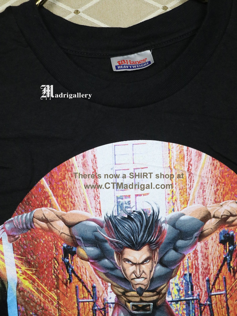 Puede incluir: Camiseta negra con un gr&aacute;fico de Wolverine, un superh&eacute;roe de c&oacute;mics, en una pose din&aacute;mica. La camiseta est&aacute; hecha de tela Hanes de peso pesado y tiene un dise&ntilde;o circular con el texto "There's now a SHIRT shop at www.CTMadrigal.com".