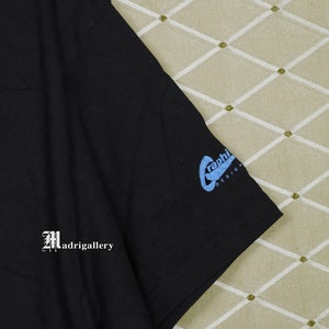 Puede incluir: Camiseta negra con un gr&aacute;fico azul de un dise&ntilde;o estilizado "graphi". La camiseta tiene un logotipo blanco "Madrigallery" en el lado izquierdo.