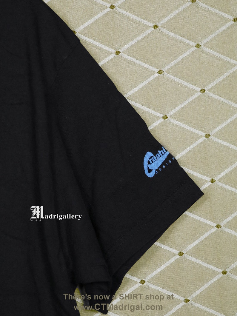 Puede incluir: Camiseta negra con un gr&aacute;fico azul de un dise&ntilde;o estilizado "graphi". La camiseta tiene un logotipo blanco "Madrigallery" en el lado izquierdo.