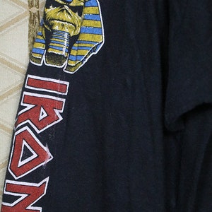 Pu&ograve; includere: Maglietta nera a maniche lunghe con un logo rosso "IRON MAIDEN" sulla manica sinistra e una grafica di una testa di faraone sulla manica destra. Il testo "THE CHURCH OF SATIN.COM" &egrave; stampato nell'angolo in basso a destra della maglietta.