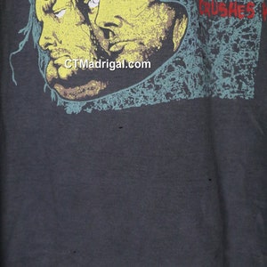 May include: A dark gray t-shirt with a faded graphic print of three faces and the text "JUSTICE CRUSHES" in red and white.