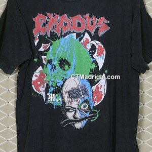 May include: Black t-shirt with a graphic print of a skull with green, blue, and red paint splatters. The text "Exodus" is printed in red and white letters above the skull. The text "Don't Puncture Container Under Pressure" is printed in white letters on the skull.