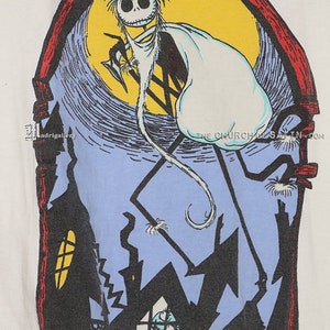Puede incluir: Una camiseta blanca con una ilustraci&oacute;n en blanco y negro de un personaje esqueleto con una capa blanca de fantasma, de pie sobre una luna azul y amarilla. El personaje sostiene una guada&ntilde;a. La ilustraci&oacute;n est&aacute; enmarcada en un arco rojo con una silueta negra de una casa y un personaje m&aacute;s peque&ntilde;o en una ventana.