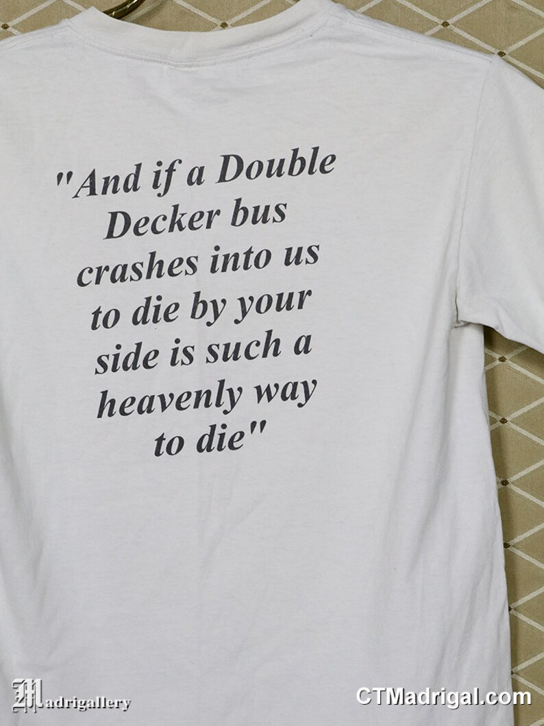 K&ouml;nnte beinhalten: Wei&szlig;es T-Shirt mit schwarzem Text. Der Text lautet: &bdquo;Und wenn uns ein Doppeldeckerbus &uuml;berf&auml;hrt, ist es so himmlisch, an deiner Seite zu sterben.&ldquo; Das Shirt hat auch die Website CTMadrigal.com.