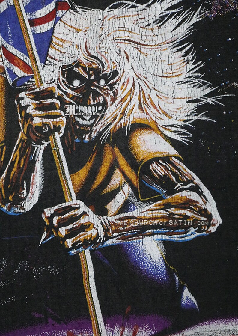 May include: A black t-shirt with a graphic print of a metal band mascot. The mascot is a monstrous figure with long white hair, holding a flag with a red, white, and blue design. The text "THE CHURCH OF SATIN.COM" is printed on the shirt.