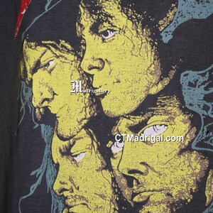 May include: A black t-shirt with a yellow and green print of four faces. The faces are of men with long hair and beards. The text "CTMadrigal.com" is printed on the shirt.