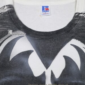 May include: White t-shirt with a black and white graphic print of a skull with wings. The shirt is made by Russell Athletic and is size L. The text "There's now a SHIRT shop at www.CTMadrigal.com" is printed on the bottom of the shirt.