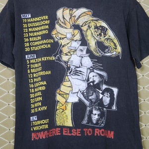 K&ouml;nnte beinhalten: Schwarzes T-Shirt mit einem Grafikdruck eines Skeletts mit einem bandagierten Kopf. Die Grafik ist von einem gelben Band mit Daten und Orten f&uuml;r eine Tour umgeben. Der Text "NOWHERE ELSE TO ROAM" ist unterhalb der Grafik gedruckt.
