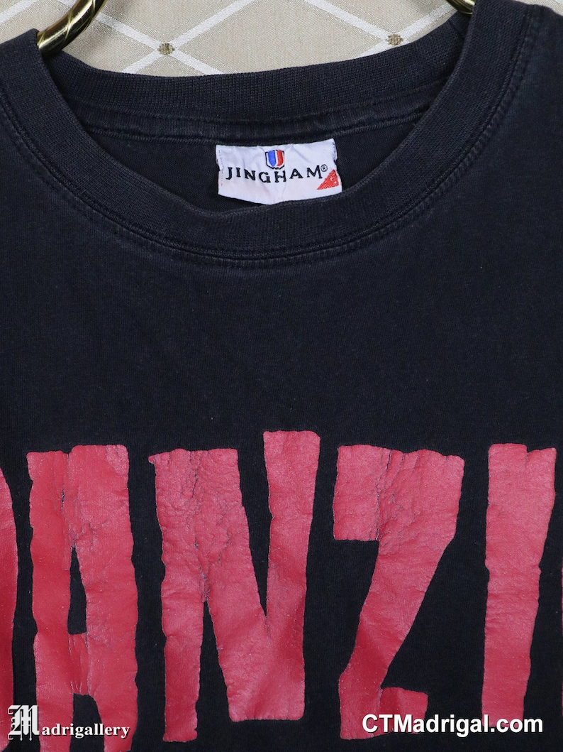 Puede incluir: Camiseta negra con un gr&aacute;fico rojo "DANZIG" impreso en la parte delantera. La camiseta est&aacute; hecha por JINGHAM.