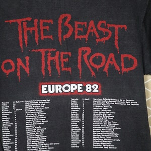 May include: Black t-shirt with a red print of "The Beast on the Road" and a tour schedule for Europe in 1982. The tour dates and locations are listed for February and April.