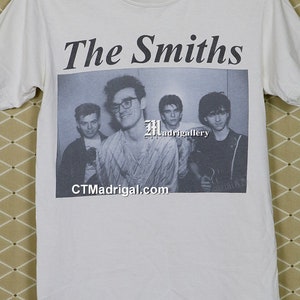 K&ouml;nnte beinhalten: Wei&szlig;es T-Shirt mit einem Schwarz-Wei&szlig;-Bild der Band The Smiths. Der Name der Band ist in fetter, schwarzer Schrift &uuml;ber dem Bild gedruckt. Die Website CTMadgrigal.com ist darunter abgebildet.