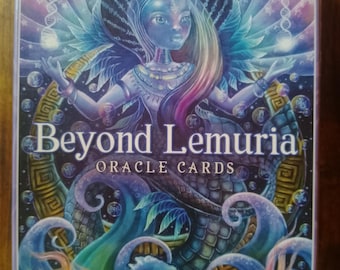 May include: A deck of oracle cards called "Beyond Lemuria" with a colorful illustration of a woman with long pink and purple hair, a blue face, and a large, green, scaly creature with a blue shell. The background is a swirling, abstract design with a purple, blue, and pink color scheme.