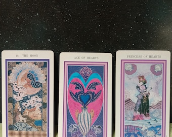 May include: Three tarot cards, The Moon, Ace of Hearts, and Princess of Hearts, with a pink rose quartz crystal in front of them. The cards are on a green and gold patterned surface.