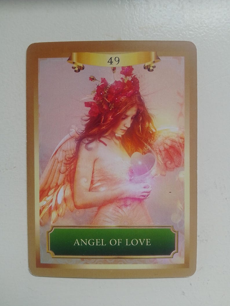 May include: Angel of Love card with a golden border and a green banner with the text "Angel of Love". The card features a woman with red hair and wings holding a pink heart.