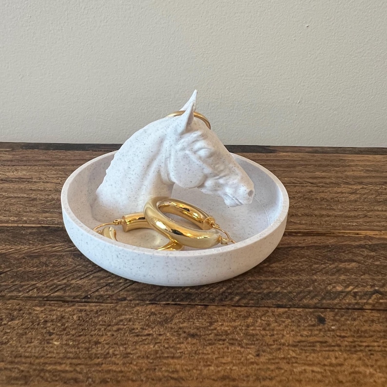 May include: White ceramic horse head ring dish with gold hoop earrings. The dish has a speckled finish.