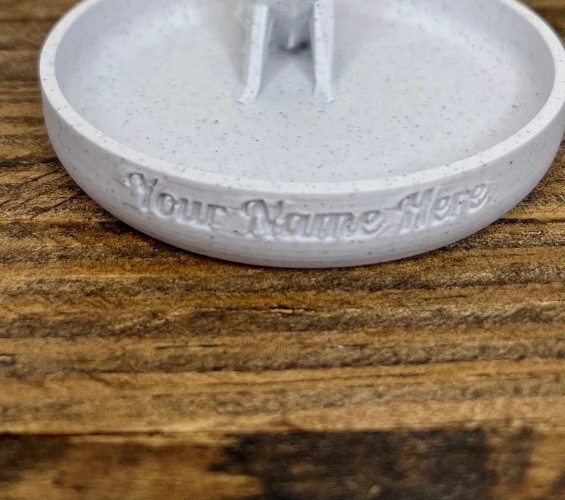 May include: White ceramic ring dish with a small raised center and the text "Your Name Here" inscribed on the edge.