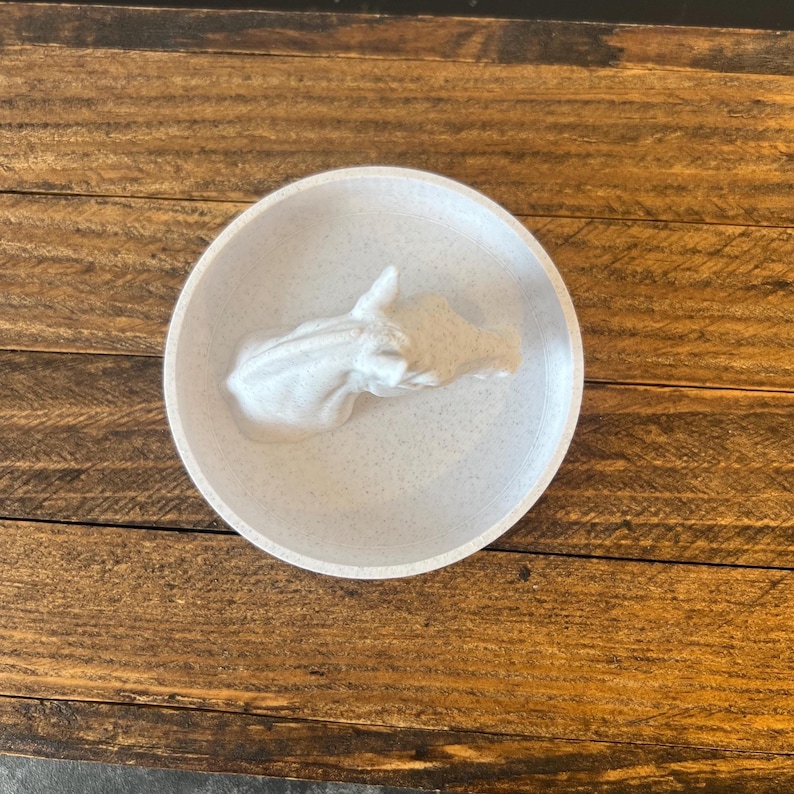 May include: White ceramic trinket dish with a white ceramic rhino sculpture inside. The dish has a speckled texture.