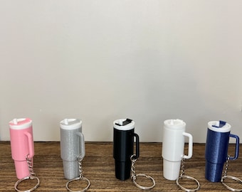 May include: Five miniature tumbler keychain replicas in pink, silver, black, white, and blue. Each keychain features a small, silver metal ring.