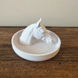 May include: White ceramic trinket dish with a horse head sculpture. The dish has a speckled finish.