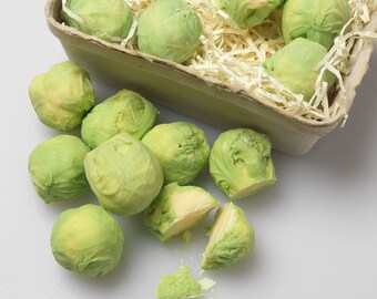 May include: A collection of green and white chocolate brussels sprout candies in a cardboard box and on a white surface.