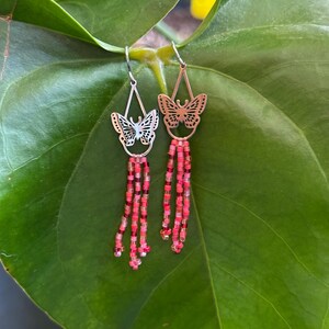 Op de afbeelding: Een paar oorhangers met een zilveren vlinderbedel en rode en transparante kralen.