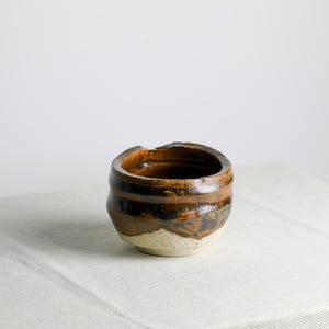 May include: A small, brown ceramic bowl with a white glaze and a slightly uneven rim. The bowl has a rustic, handmade look.