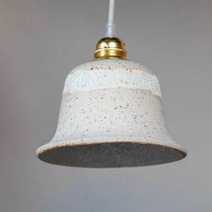 Könnte beinhalten: Eine weiße Keramik-Pendelleuchte mit gesprenkeltem Finish und einem goldenen Metall-Oberteil. Die Leuchte hat eine Glockenform und eine weiße Glasur.