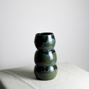 May include: A green and blue ceramic vase with a unique, stacked design. The vase is made of three stacked, rounded sections.
