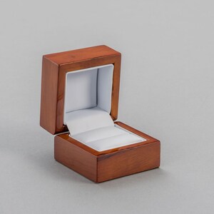 May include: A wooden ring box with a hinged lid and a white velvet interior. The box is open and the lid is propped up.