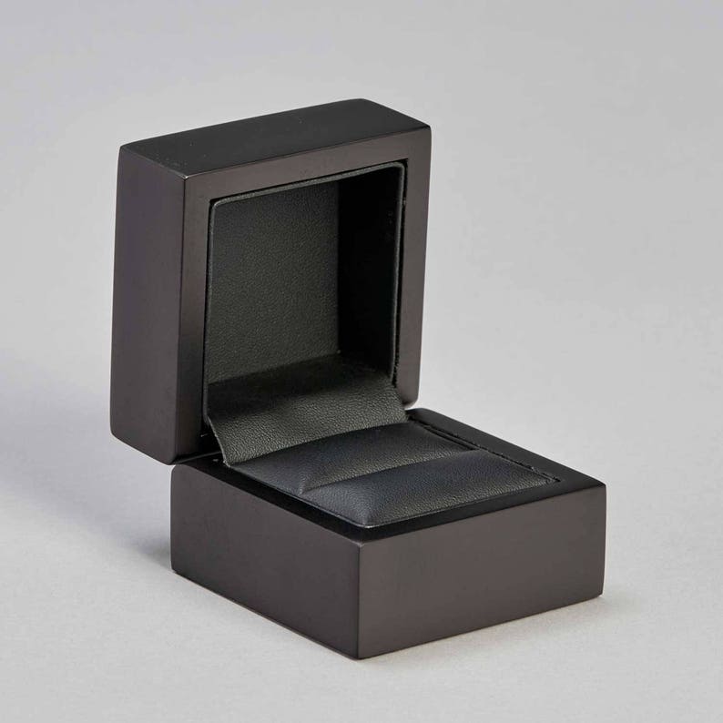 May include: A black ring box with a velvet interior. The box is open and the lid is propped up.