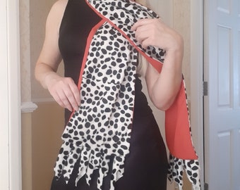 May include: A black and white dalmatian print scarf with a red trim. The scarf is tied around the neck and hangs down the front of the body.