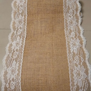 Puede incluir: Un camino de mesa de arpillera marrón con ribete de encaje blanco a ambos lados.