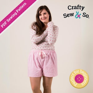 May include: A woman wearing a light pink pajama set. The long-sleeved top has a small floral pattern. The shorts are pink and white gingham with a pink drawstring. The image includes the text "PDF Sewing Pattern" and the logo "Crafty Sew & So."