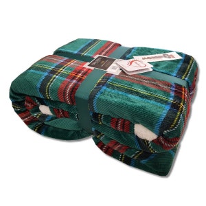 Può includere: Coperta a quadri verde piegata con accenti rossi, blu e gialli. La coperta è legata con un nastro verde e ha un lato inferiore bianco e soffice. I tag sono attaccati al nastro.