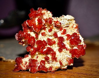 May include: A close-up of a mineral specimen featuring vibrant, crystalline, red-orange formations clustered on a beige matrix. The crystals have a sparkling, reflective quality, contrasting with the rougher texture of the base.