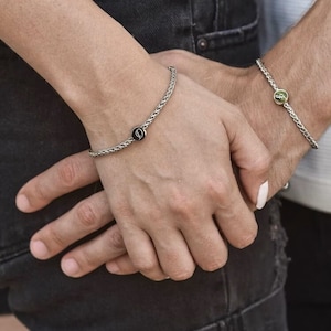 May include: Two silver chain bracelets with small round charms. One charm has a black background with a white letter "D" and the other charm has a green background with a white letter "S".