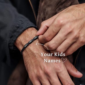 May include: A black bracelet with the names "Emma", "Jack", and "Liv" on it. The bracelet is worn on a person's wrist. "Your Kids Names" is written on the image.