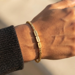 May include: A gold-toned wheat chain bracelet featuring three small rectangular charms. Each charm is engraved with a name: Scarlett, Annabelle, and Chloe. The bracelet has a polished metallic finish and a secure clasp mechanism.