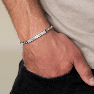 May include: A silver chain bracelet with a personalized bar charm engraved with the names "David" and "Adele" separated by a heart symbol.