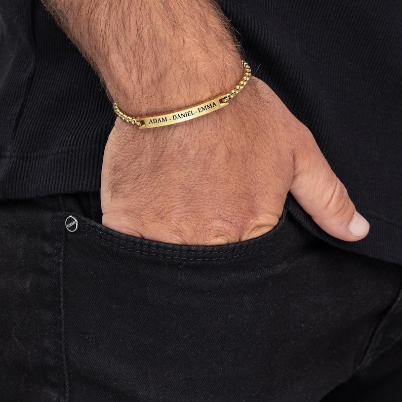 May include: A gold chain bracelet with a rectangular nameplate engraved with the names "ADAM, DANIEL, EMMA".