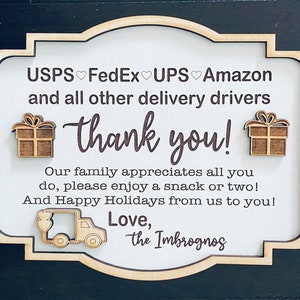 Può includere: Un cartello di legno con sfondo bianco e lettere marroni che dice "USPS FedEx UPS Amazon e tutti gli altri fattorini grazie! La nostra famiglia apprezza tutto quello che fai, prenditi pure uno spuntino o due! E buone feste da parte nostra a te! Con affetto, gli Imbrognos". Il cartello ha due piccole scatole regalo di legno e un camioncino di consegna di legno.