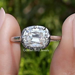 Op de afbeelding: Een zilveren ring met een grote, heldere, ovale edelsteen gezet in een bezel setting. De ring wordt gedragen aan een vinger, met een wazige achtergrond.