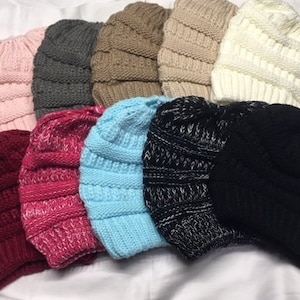May include: Assortment of ten knitted beanie hats in various colors, including pink, gray, brown, white, blue, red, and black. The hats are made of a soft, cozy material and have a slouchy fit.