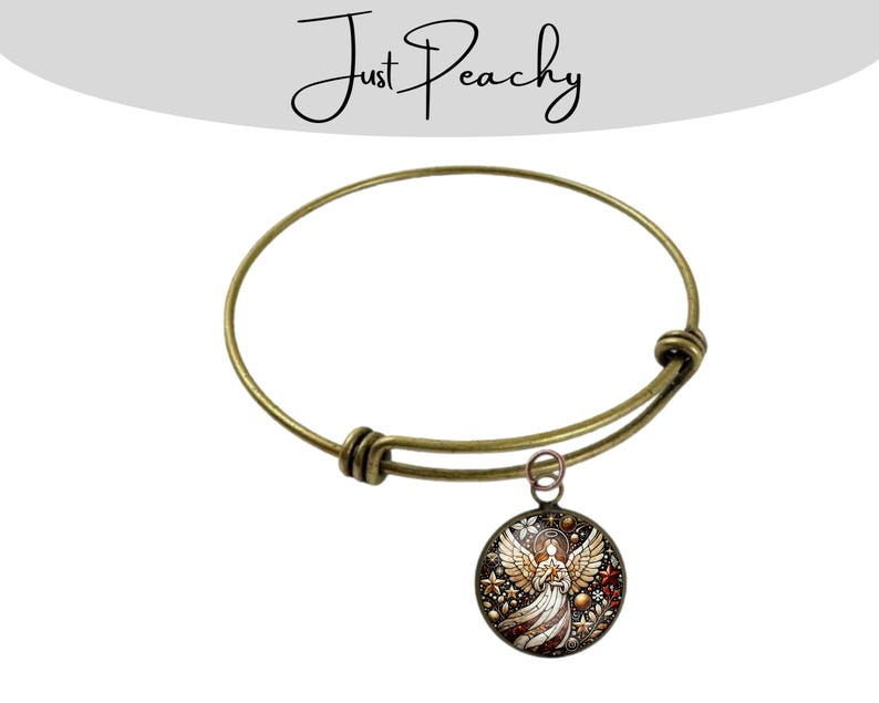 Op de afbeelding: Antiek goudkleurige verstelbare armband met een ronde bedel. De bedel heeft een gedetailleerd engelontwerp met rode, witte en gouden accenten. De armband heeft een eenvoudig, elegant ontwerp.