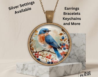May include: A round bronze-toned pendant necklace featuring a bluebird perched on a branch with red berries. Text on the image reads: Silver Settings Available, Earrings, Bracelets, Keychains and More, and Just Peachy.