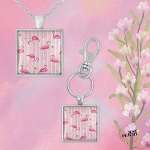 May include: A silver necklace pendant and keychain featuring a pink flamingo pattern on a square background with white stripes. The background is a soft pink. The keychain has a silver clasp.